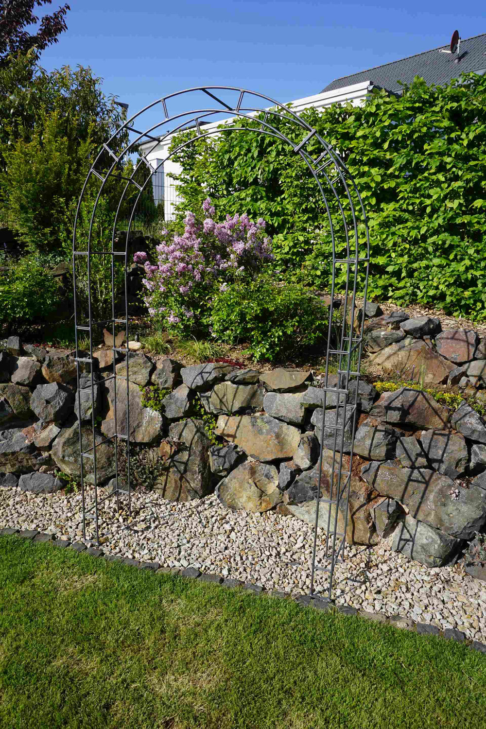 Rosenbogen Cremona vor einer Steinmauer | Pulverbeschichtet anthrazit Rosenbogen Cremona vor einer Steinmauer | Pulverbeschichtet anthrazit