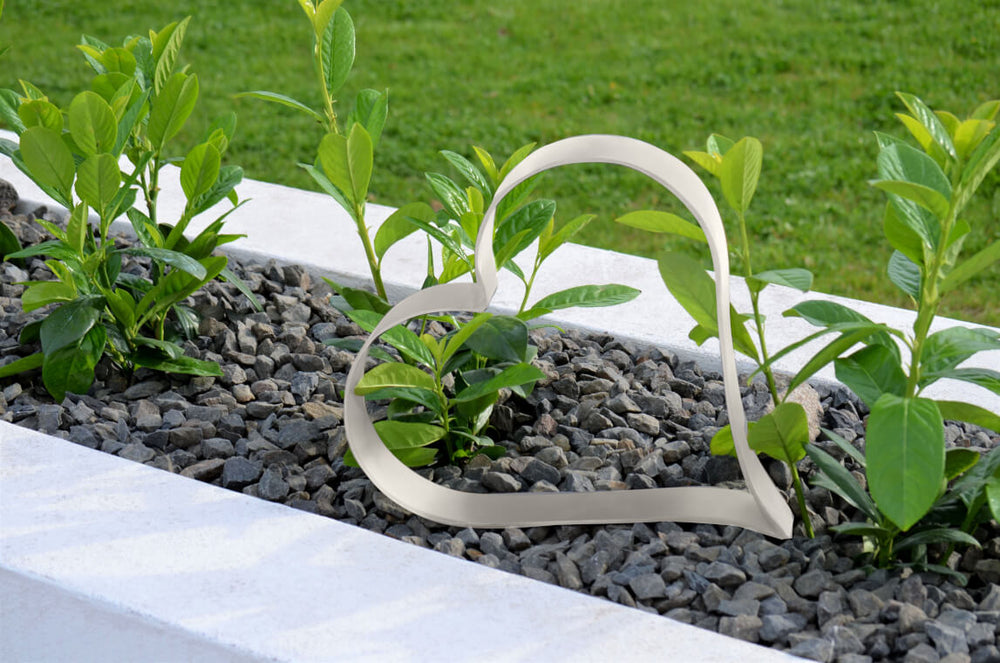 Metallherz Biella in pulverbeschichtet Sonderfarbe RAL 9001 Cremeweiß auf bepflanzter Beetoberfläche mit Steinen Metallherz Biella in pulverbeschichtet Sonderfarbe RAL 9001 Cremeweiß auf bepflanzter Beetoberfläche mit Steinen