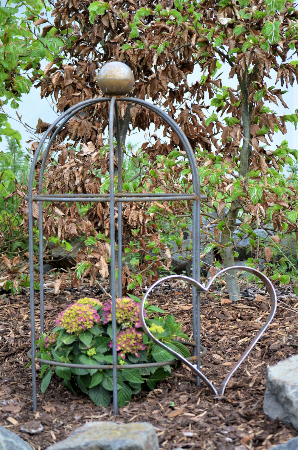 Metallherz Biella neben Rankobelisk vor grünen Bäumen, unbeschichtet Metallherz Biella neben Rankobelisk vor grünen Bäumen, unbeschichtet