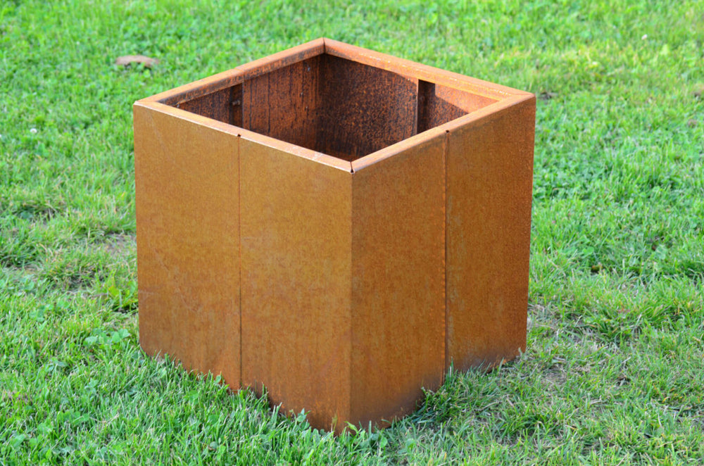 Pflanzkübel Vernazza in 40x40x40 cm aus Cortenstahl unbepflanzt in einem grünen Garten Pflanzkübel Vernazza in 40x40x40 cm aus Cortenstahl unbepflanzt in einem grünen Garten