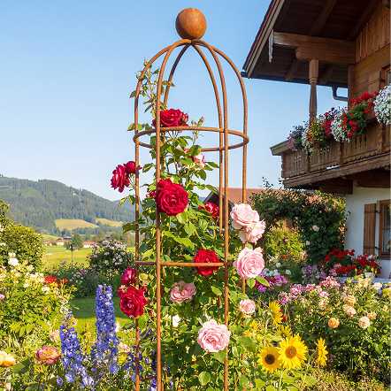Rankobelisk Messina unbeschichtet in Rostoptik mit Rosen berankt in einem ländlichen Garten mit vielen blühenden Blumen.