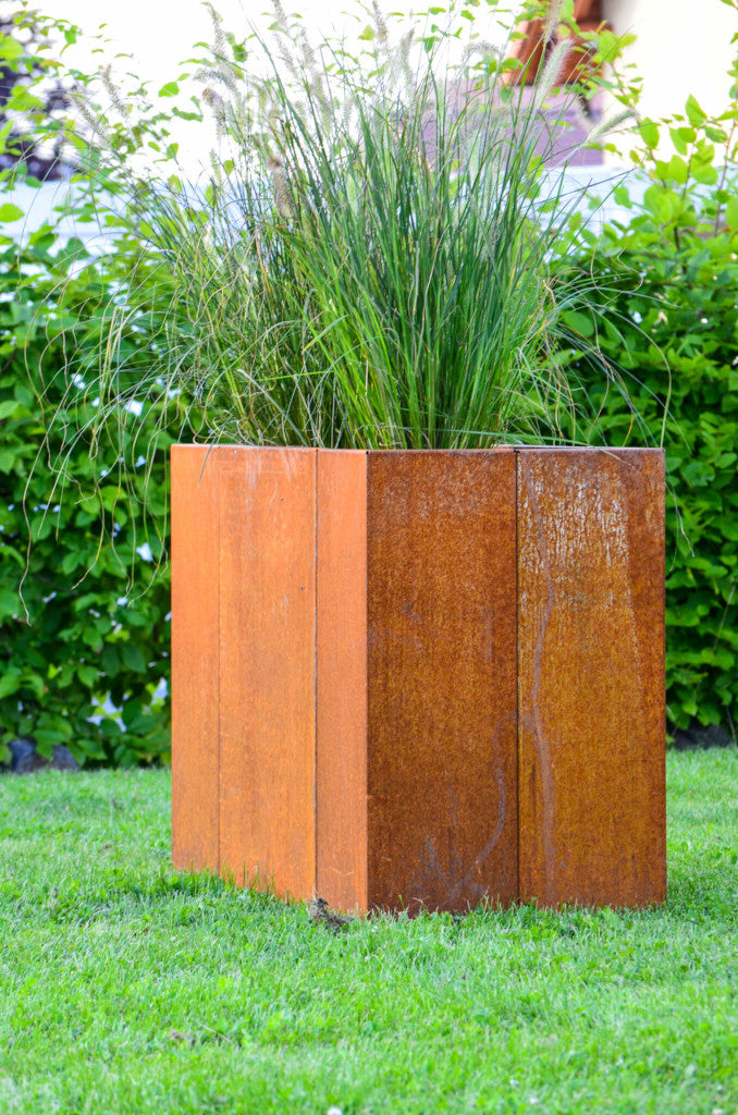 Hochbeet Monterosso 45x135x68 in Cortenstahl bepflanzt vor einer grünen Hecke